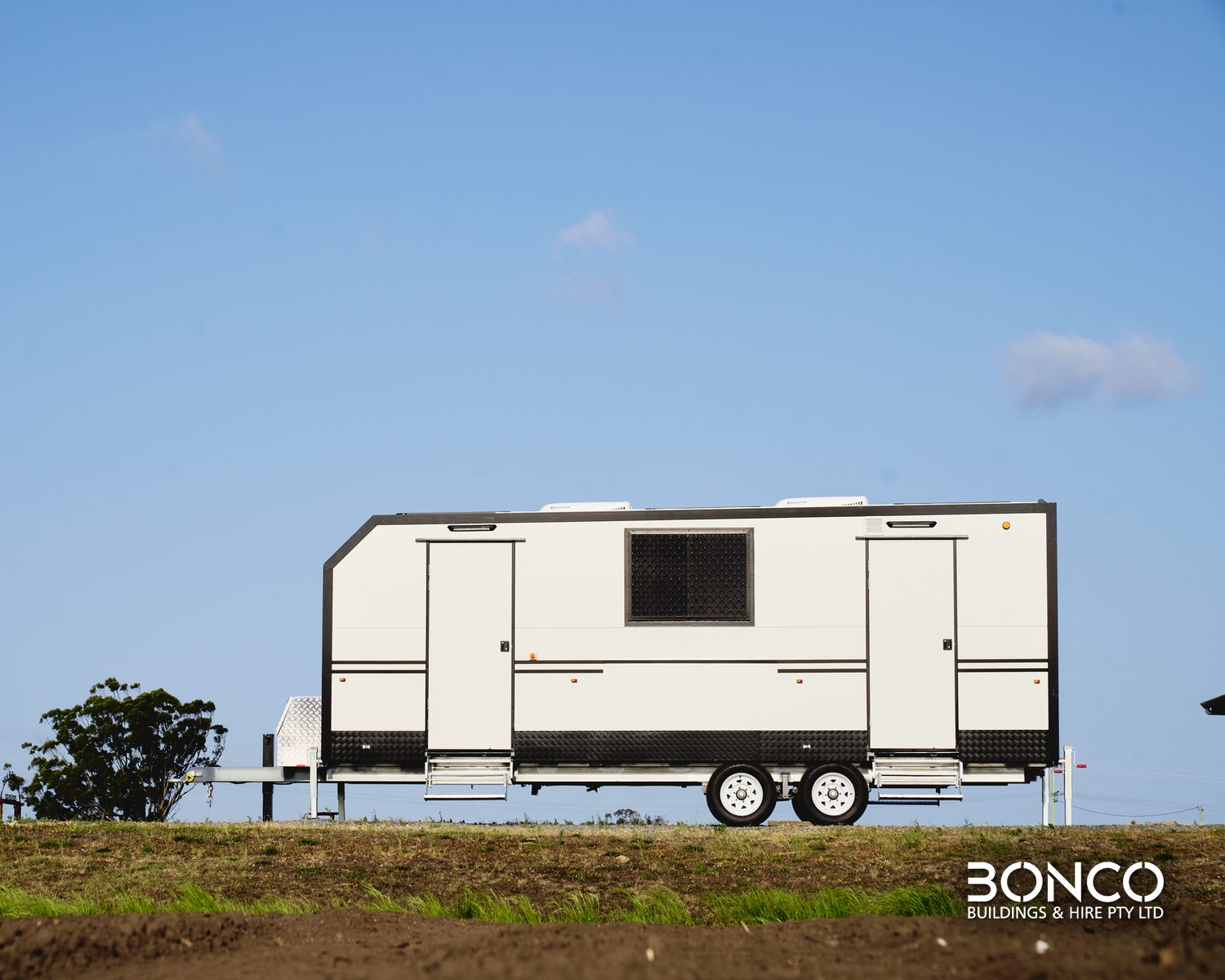 Bonco mobile crib room hire – side view of a white dual-axle crib room trailer with two entry doors and fold-down steps